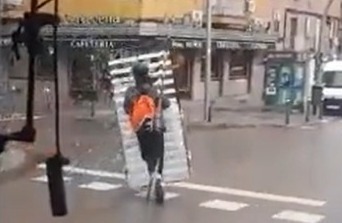 Un hombre pasea subido a un patinete con un somier